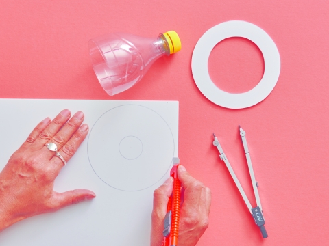 Zweitletzte Plastikschale ausmessen. Auf dem Hartschaum zwei gleich grosse Kreise aufzeichnen, ausschneiden. Bei einem Ring für die Fassung ein Loch ausschneiden. Der zweite Kreis wird mit dem Durchmesser der PET-Flasche ausgeschnitten.