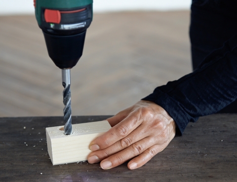 Mit einer Bohrmaschine werden zwei Löcher in das Holz gebohrt