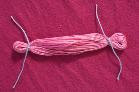 Für die Arme wiederum Garn um den Karton wickeln und danach vorsichtig abnehmen. An beiden Enden des Stranges ca. 1 cm mit Garn abbinden für die Hände.